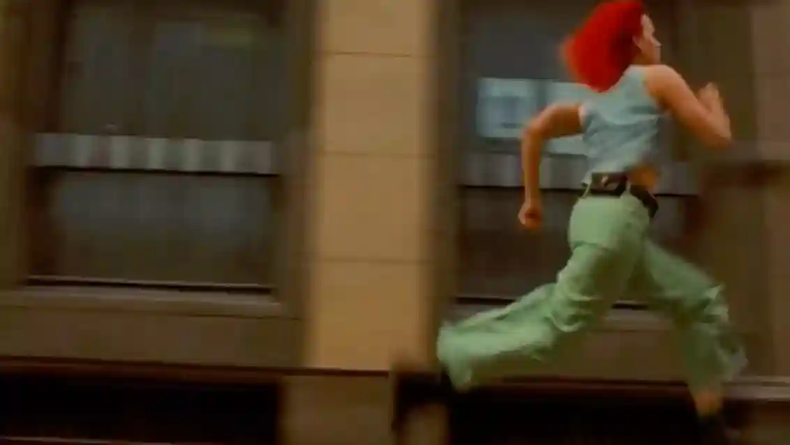 لقطة من فيلم Run Lola Run تظهر البطلة أثناء الجري في برلين وتوفر فرصة لتعلم الألمانية الحديثة قائمة تضم أفضل 10 أفلام لتعلم اللغة الألمانية للمبتدئين والمتقدمين مع المميزات والعيوب ونصائح عملية لتحسين الاستماع والمفردات بطريقة ممتعة وفعالة.