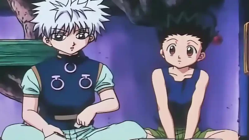 لقطة شاشة كلاسيكية من أنمي "Hunter x Hunter" (القناص) تظهر غون فريكس ذو الشعر الأسود واقفاً، وصديقه العزيز كيلوا زولديك ذو الشعر الأبيض جالساً، وهما ينظران باهتمام تحت ضوء خافت في غرفة أرجوانية.